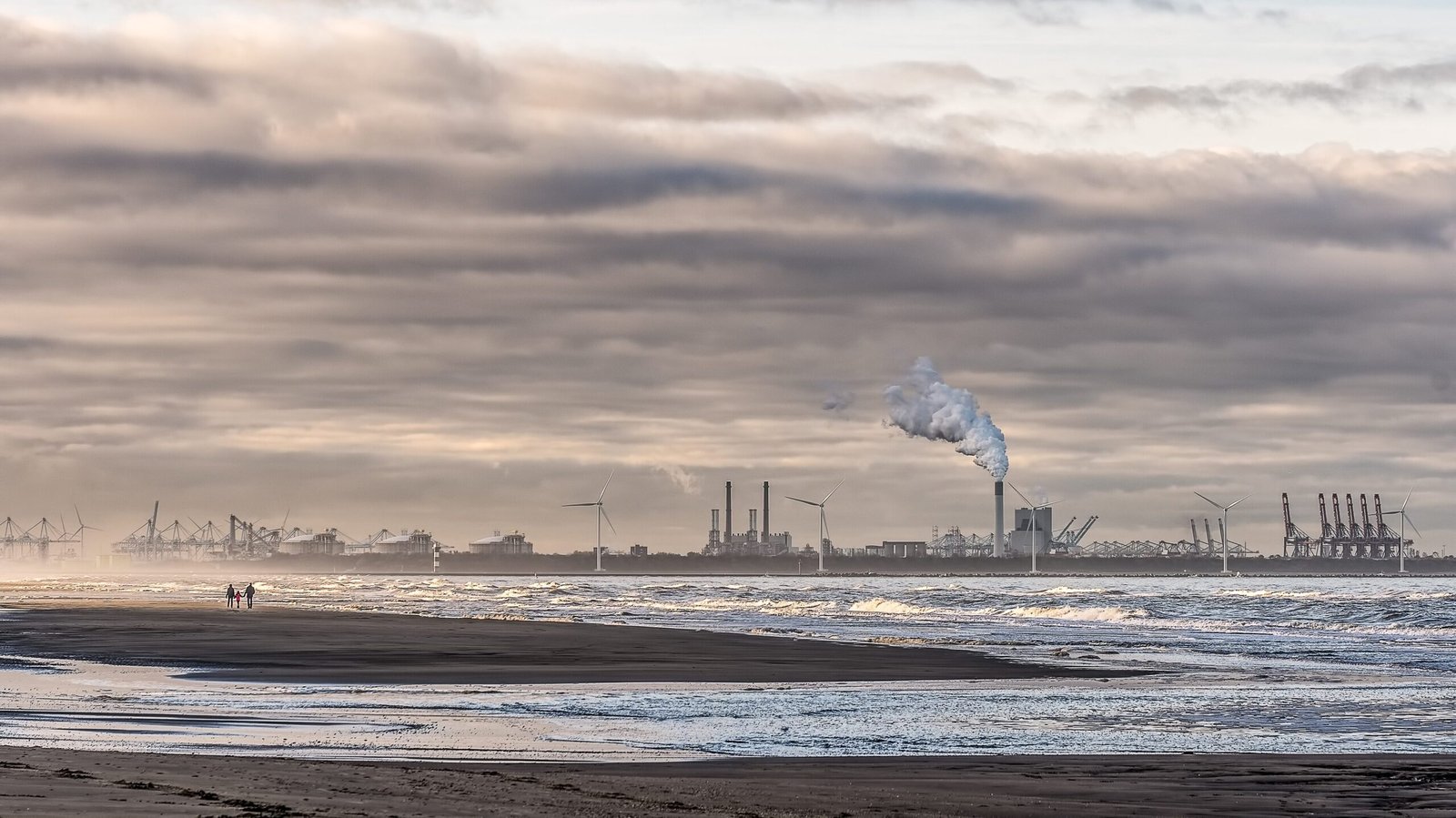 Jakarta Turun ke Peringkat 7 Kota dengan Udara Terburuk Dunia beautiful shot of a sea with windmills and factory in the distance under a cloudy sky